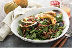 a white bowl filled with green salad and topped with nuts, pumpkins and pomegranate