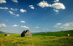 an old barn sits in the middle of a green field with bales on it