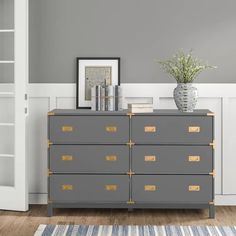 a gray dresser with gold handles and drawers in a room next to a white door