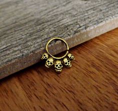a pair of gold skull rings sitting on top of a wooden table next to a piece of wood