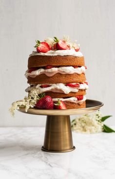 a cake with strawberries and cream frosting on a gold plate next to flowers