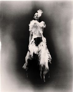 black and white photograph of a woman with feathers on her body, standing in front of a dark background