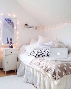 a bed with white sheets and pillows in a room that has lights on the walls