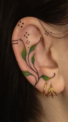 a woman's ear with green leaves and dots on the inside of her ear