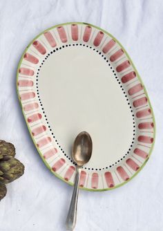 a pink and green plate with a spoon on it next to a flower pot or plant