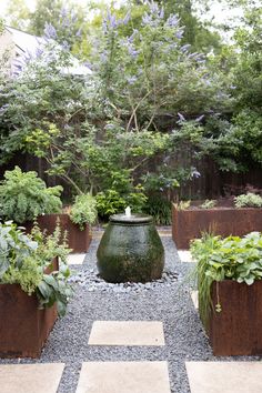 an outdoor garden with several planters and gravel path leading to the water feature in the center