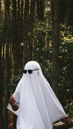 a person in a white robe and sunglasses walking through the woods