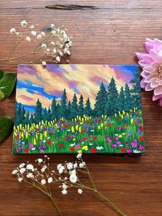 an acrylic painting of flowers and trees on a wooden table next to a pink flower