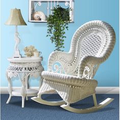 a wicker rocking chair next to a small table with flowers and potted plant