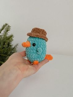 a hand holding a small blue crocheted bird with a hat on it's head