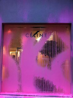 a pink and purple store front window with the reflection of a woman's face on it