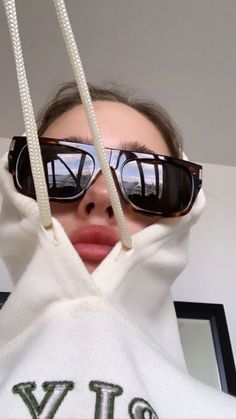 a woman with sunglasses on her head wearing a white hoodie and holding up two pairs of glasses