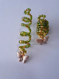two gold and green beaded earrings sitting on top of a white table next to each other