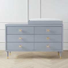 a grey dresser with gold handles and knobs on the drawers, against a white wall