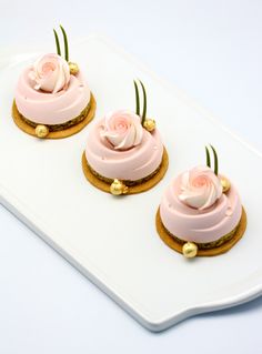 three cookies with pink frosting and gold decorations on a white platter next to each other