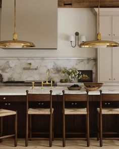 a kitchen with marble counter tops and wooden chairs in front of an island that has gold lights hanging from the ceiling