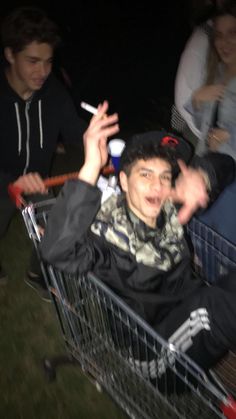 a man sitting in a shopping cart with his hand up to the side and people standing around him