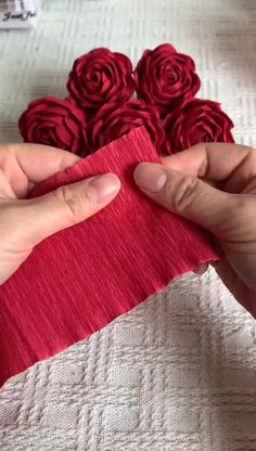 two hands are stitching fabric together with red flowers on the tablecloth behind them