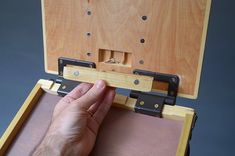a hand is opening the top of a wooden box with latches on both sides