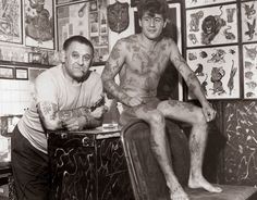two men with tattoos on their bodies sitting in a room