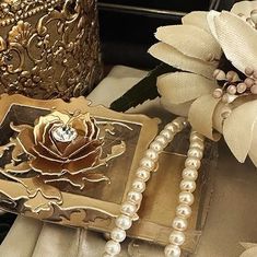 some pearls and flowers are sitting on a table next to a gold vase with a flower in it