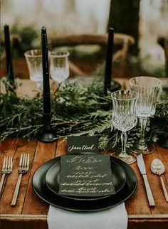the table is set with black plates, silverware and greenery for an elegant dinner