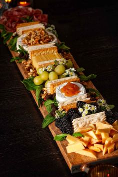 an assortment of cheeses, fruits and crackers are arranged on a wooden platter