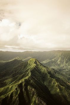 an aerial view of green mountains under a cloudy sky