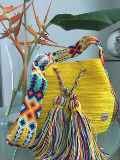a yellow handbag with tassels on it sitting next to a flower vase