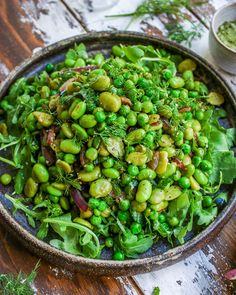 a bowl filled with peas and greens on top of a wooden table next to other dishes