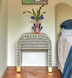 a room with a bed and a painting on the wall next to a table that has flowers in it