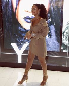 a woman is standing in front of a poster wearing high heeled sandals and an off the shoulder dress