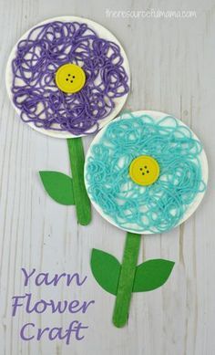 two paper flowers made with yarn and buttons on white wooden background, text yarn flower craft
