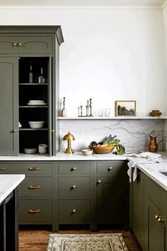 a kitchen with green cabinets and marble counter tops, gold pulls on the cupboards
