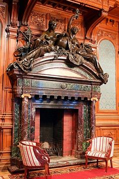 an ornate fireplace with two chairs in front of it and a statue on the mantle