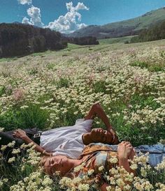 a man laying in the middle of a field with white flowers on his chest and head