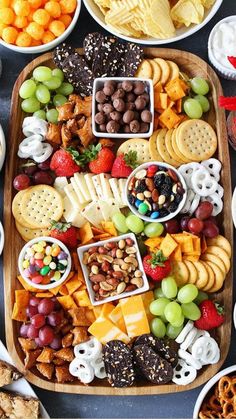 a platter filled with cheese, crackers, fruit and nuts next to other snacks