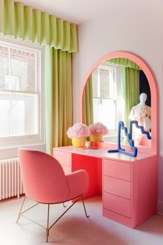a pink desk with a mirror, chair and vases in front of the window