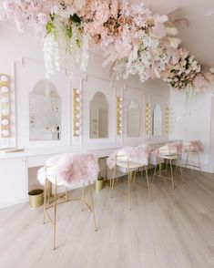 the interior of a hair salon with pink flowers hanging from the ceiling and gold chairs