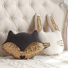 two pillows with gold sequins on top of a white headboard and an upholstered bed