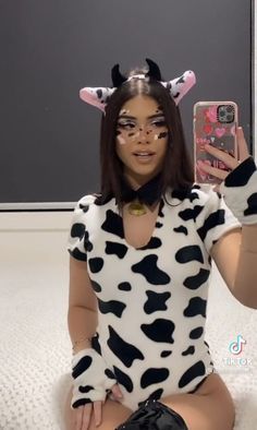 a woman in a cow costume is holding up her cell phone to take a selfie
