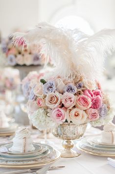 a vase filled with lots of flowers and feathers on top of a table next to plates