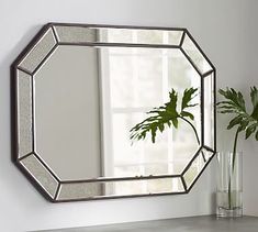 a mirror sitting on top of a table next to a vase with a plant in it