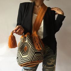 a woman wearing ripped jeans and a black blazer holding a woven bag with tassels