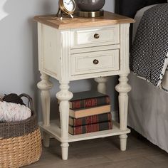 a white nightstand with books and a clock on it's side table next to a bed