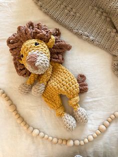 a crocheted lion laying on top of a bed next to a beaded necklace