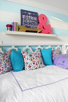 a white bed topped with lots of pillows next to a shelf filled with colorful books