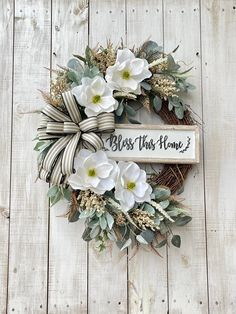 a wreath with white flowers and greenery tied to it on a wooden background that says, bess this home