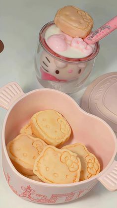 hello kitty cookies are in a pink bowl next to a plastic container with the lid open