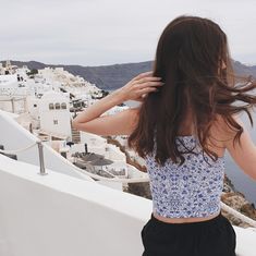 a woman standing on top of a white building next to the ocean with her hair blowing in the wind